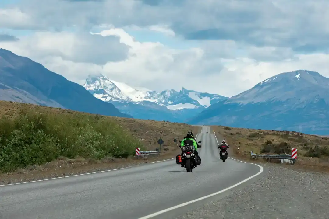 Two motorcycles on a paved road with snow-capped Andes peaks ahead