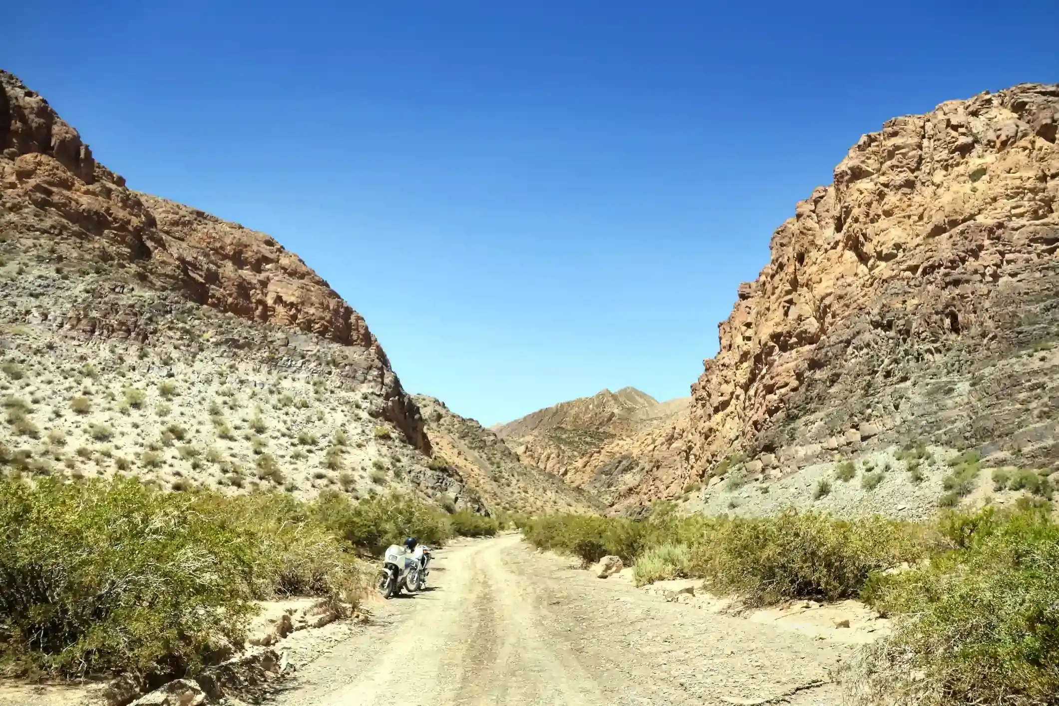 Motorcycle on a gravel road through a rocky Patagonian canyon under clear blue sky.