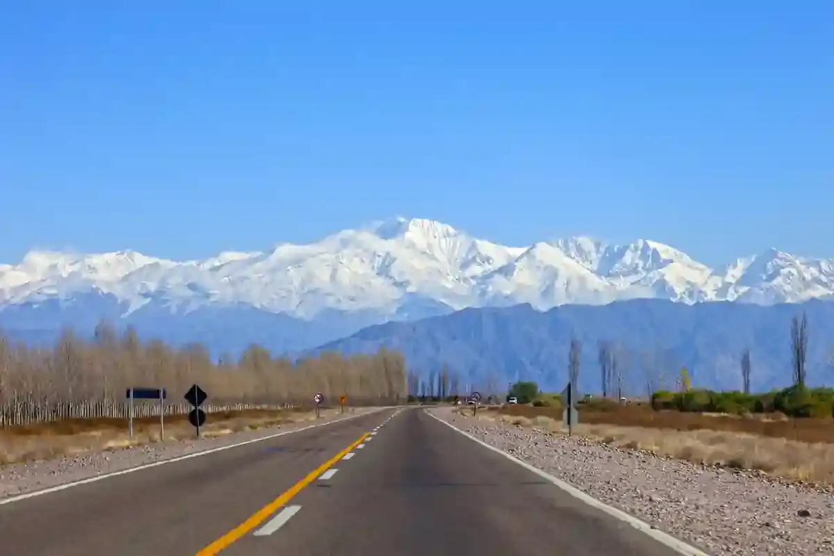 An empty paved highway heads toward the snow-covered Andes near Mendoza, Argentina.