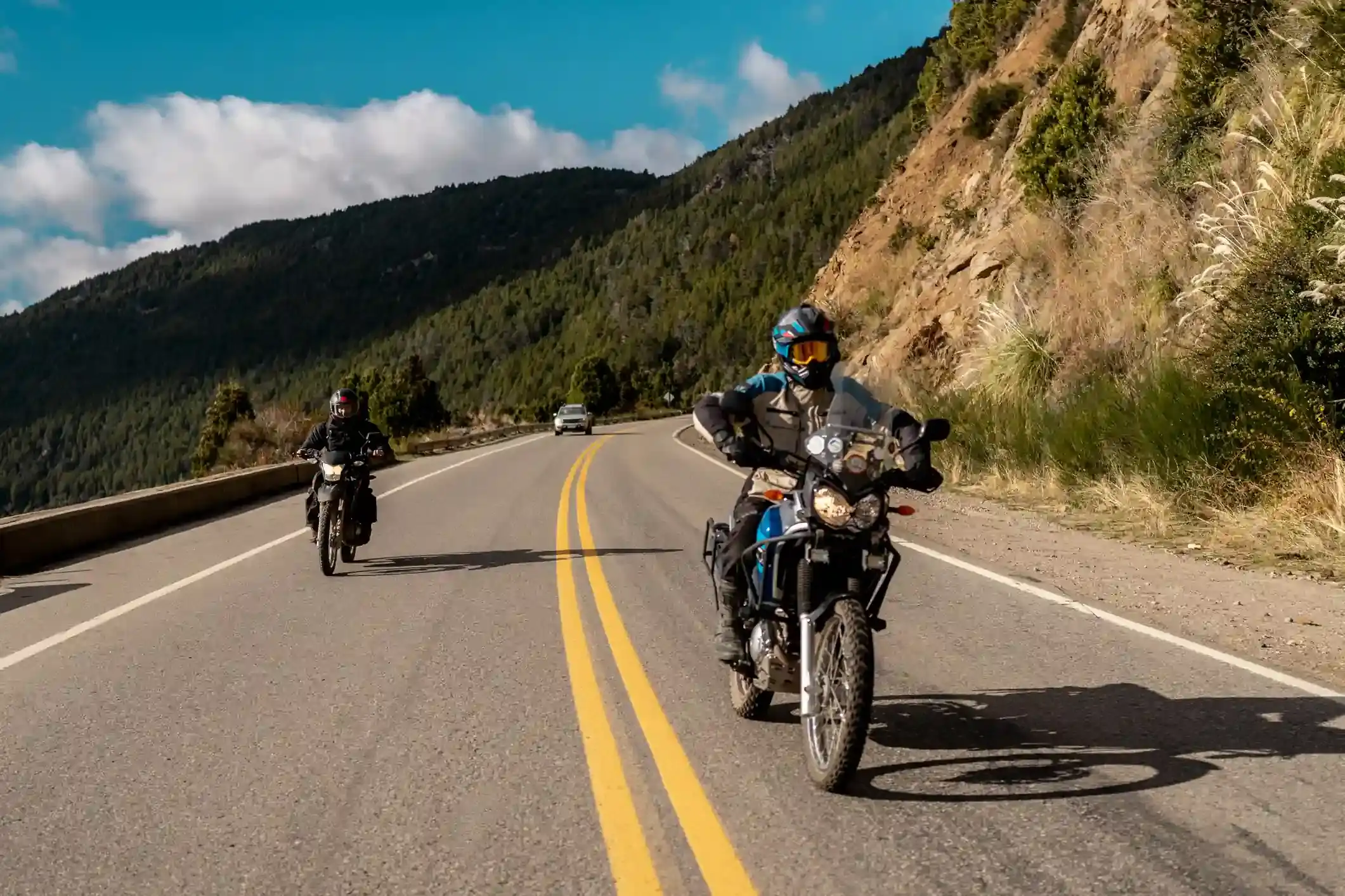 Two adventure motorcycles riding on a paved road through forested Patagonian mountains in Argentina.